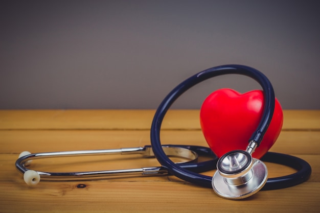 Close up red heart and steythoscope on old wood table