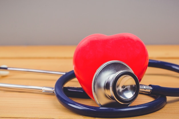 Close up red heart and steythoscope on old wood table