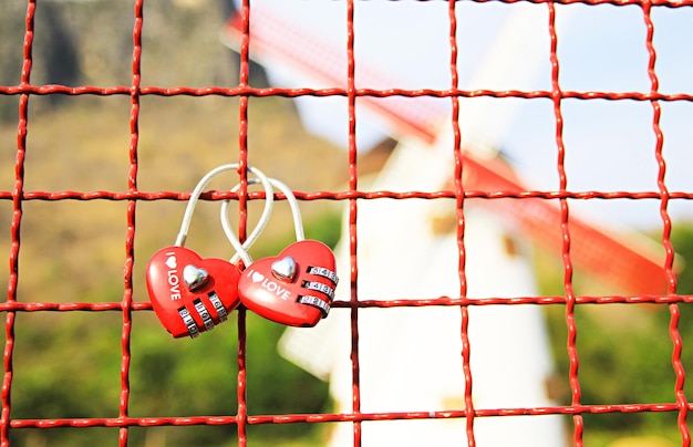 Photo close up red heartshaped lock padlock on the steel grate with a young couple in tourist attractions