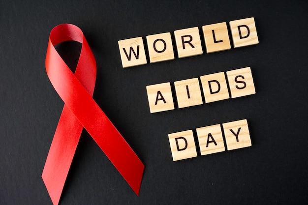 Close-up of red ribbon by world aids day text over black background