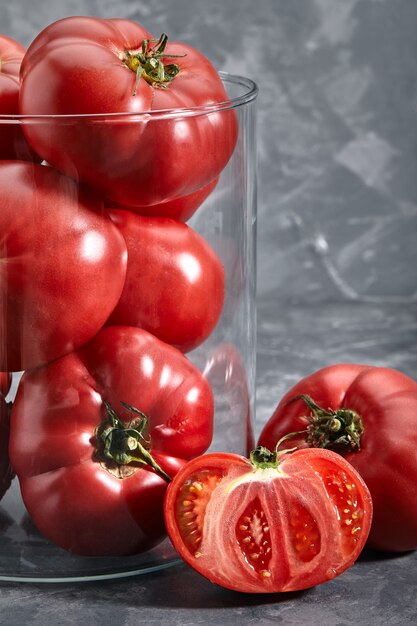 Close-up of red tomatoes with a glass vase on a gray background.