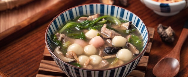 Close up of red and white tangyuan (tang yuan, glutinous rice dumpling balls) with savory soup in a bowl on wooden table background for Winter solstice festival food.