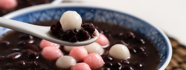 Primo piano di tangyuan rosso e bianco (tang yuan, palline di gnocco di riso glutinoso) con zuppa di fagioli rossi dolce in una ciotola su sfondo bianco da tavola per il cibo del festival del solstizio d'inverno.