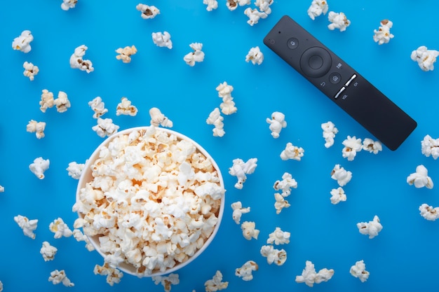 Close-up of remote control and testy warm spilled popcorn viewed from above on blue