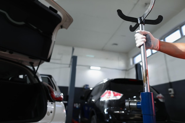 Close-up of repair service worker hold metal stand near open automobile hood. Garage with parking for fixing damaged cars. Maintenance, pit stop concept