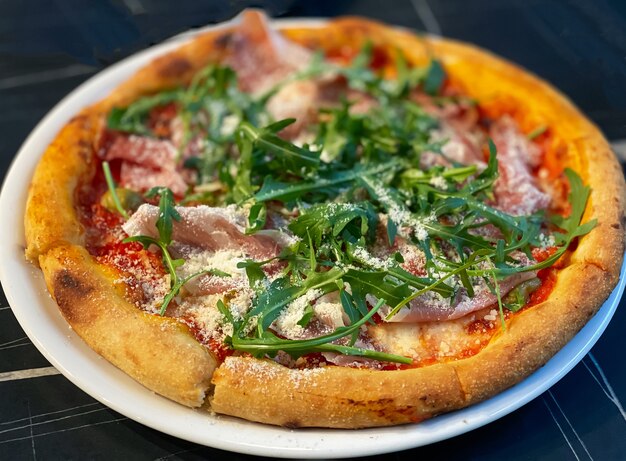 Close-up on a restaurant table pizza with prosciutto, arugula and parmesan cheese.  Food concept.