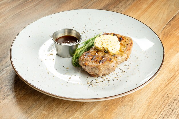 Close-up ribeye steak met mosterdboter, rozemarijn en rode saus op een witte plaat op houten