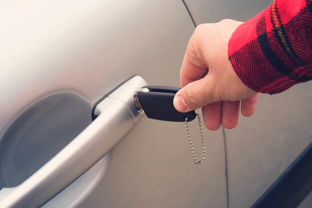 車のドアの穴のキーを回して右の男性の手のクローズアップ。男は鍵を使って新しい車を開けます。レンタカー。運転免許を取得する。運転の準備をしています。機械的なロック解除。