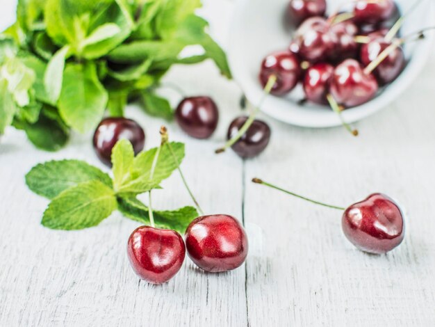 Close-up on ripe sweet cherry berry with mint on white wooden background