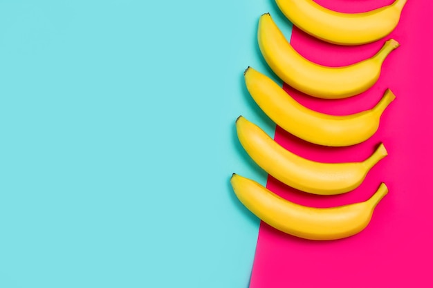 Close-up of ripe yellow bananas on a colorful of pink and blue background. Top view