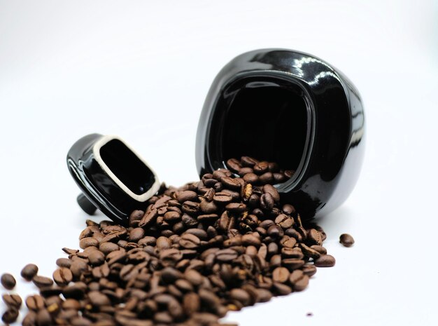 Photo close-up of roasted coffee beans spilling from container over white background