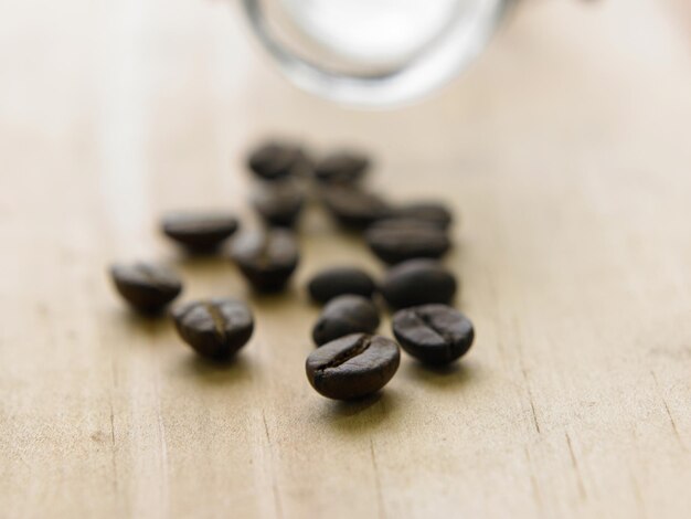 Photo close-up of roasted coffee beans spilling from jar on table