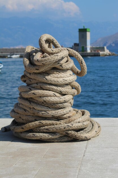 Photo close-up of rope tied to bollard at harbor against sky