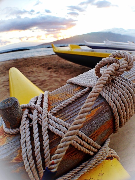 Photo close-up of rope tied to canoe on beach against sky