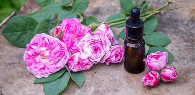 Primo piano della bottiglia di olio essenziale di rosa con foglie che cadono su fondo di legno. messa a fuoco selettiva