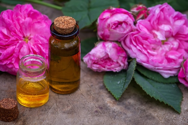 Close-up of rose essential oil bottle with falling leaves on wooden background. Selective focus