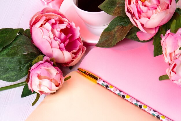 Close-up rose flowers with pen and cup of coffee. Open pink notepad and pencil.