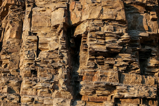 Close-up rufous stony wall with layered uneven hollowed-out surface.