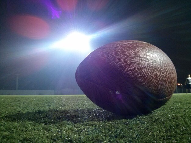 Close-up of rugby ball on field against illuminated floodlight at night