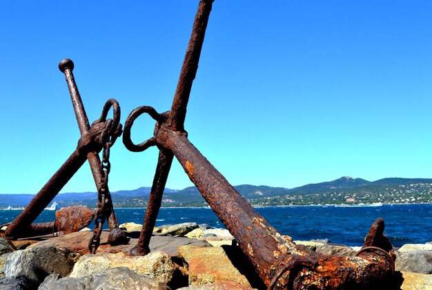 Close-up of rusty metal by sea against clear blue sky