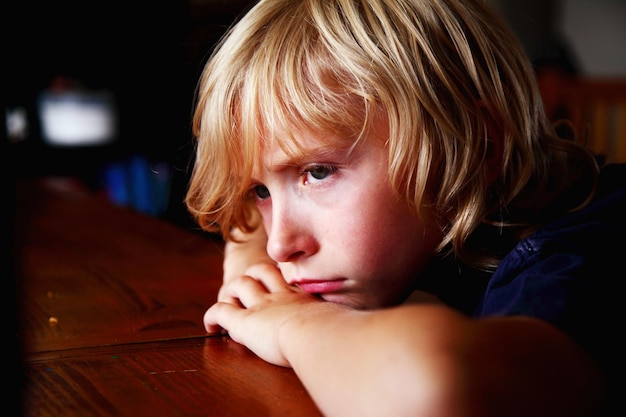 Close-up of sad boy leaning on table at home