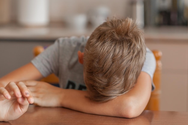Close-up of sad boy sleeping on table at home