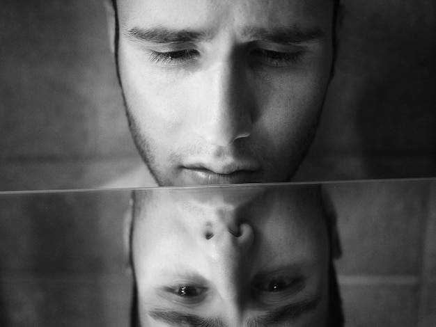 Photo close-up of sad shirtless man looking at his reflection in mirror