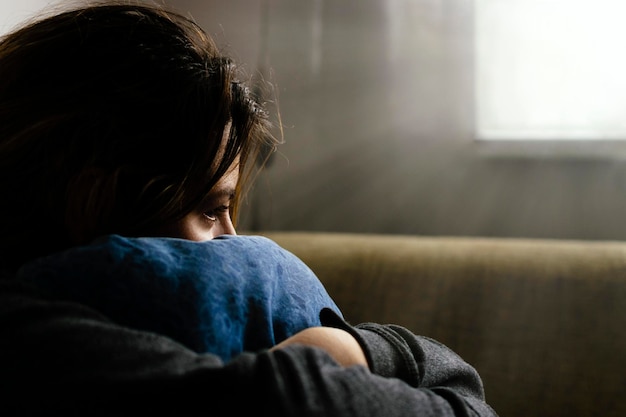 close-up of sad woman hugging cushion while sitting at home