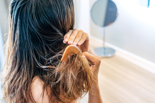 Close up of sad young Asian woman brush her damaged and tangled wet hair