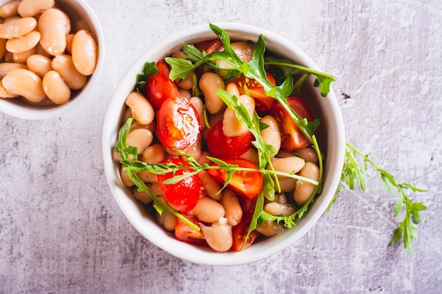 Close up of salad of canned white beans cherry tomatoes and arugula in a bowl top view