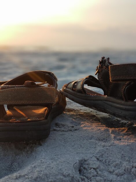 Photo close-up of sandals on rock at beach against sky during sunset