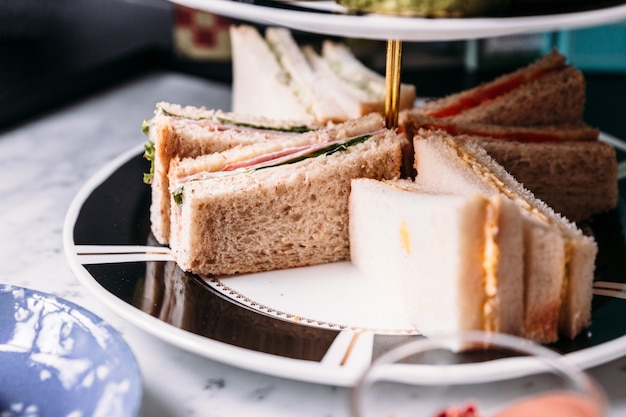 Close up sandwiches on 3 tier ceramic serving tray for eating with hot tea.