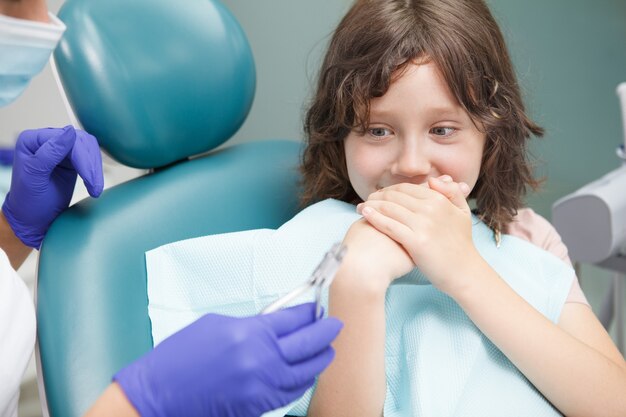 Close up of a scared young boy covering his mouth with his hands, afraid of dental treatment