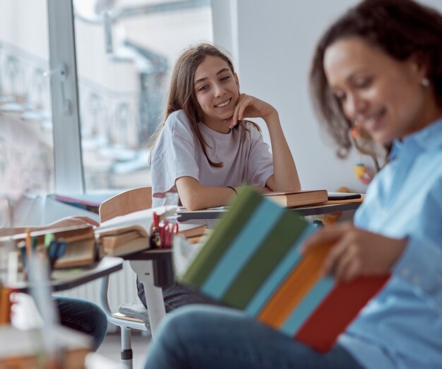 Foto close-up schattig schoolmeisje glimlachen terwijl jonge tutor haar leest. basisschoolkinderen zittend op een bureau in de klas.