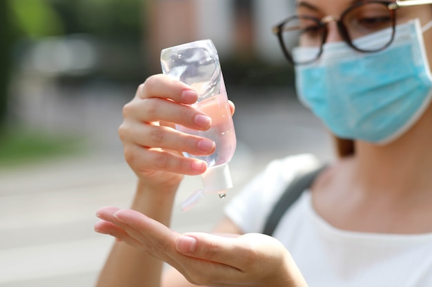 Chiuda su della ragazza della scuola con la maschera medica facendo uso del gel del prodotto disinfettante della mano in via della città. concetto di antisettico, igiene e sanità. concentrarsi sulle mani.