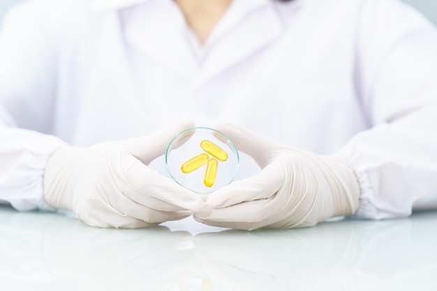 Close up Scientist hands putting in nitrile latex gloves holding Omega 3 capsule in labcoat doing experiments in lab