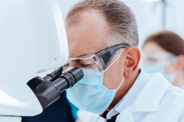 Close up scientist in a protective mask looking through a microscope science and health protection