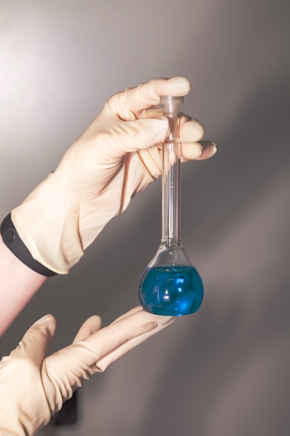 Foto primo piano della mano di uno scienziato che tiene una boccetta di liquido chimico blu. vetreria di laboratorio nel laboratorio chimico per lo sfondo. concetto di ricerca e sviluppo in un laboratorio scientifico