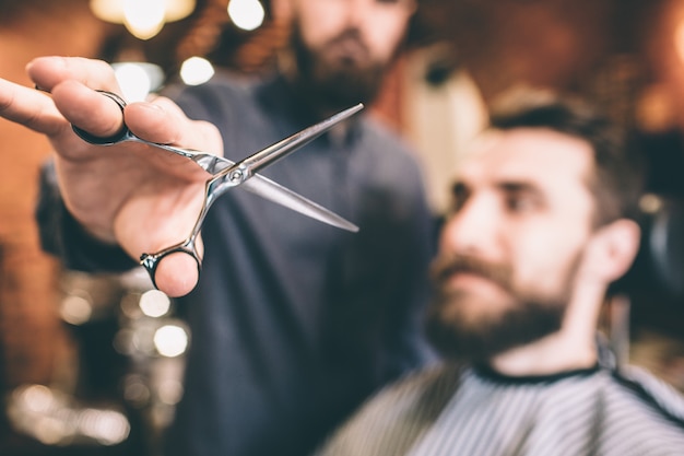 Close up of scissors that the hairstylist is holding. The scissors are opened. The customer is ready for the procedure.