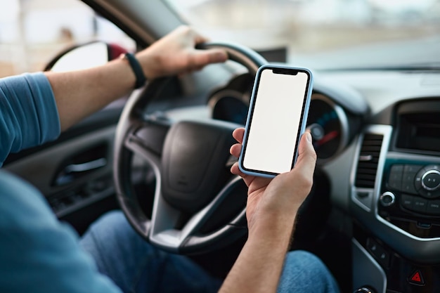 Foto chiudere il telefono cellulare mockup con schermo vuoto nelle mani di un conducente uomo irriconoscibile in un'auto