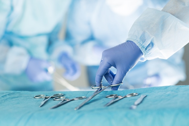 Close-up of scrub nurse taking medical instruments for operation with colleagues performing