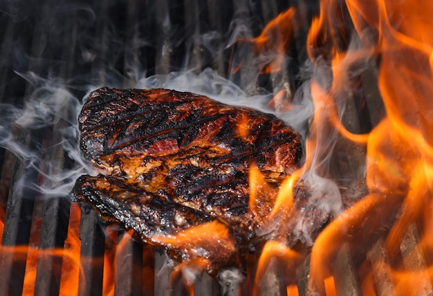 close up searing smoking ribeye beef steaks on open fire outdoor grill with cast iron metal grate