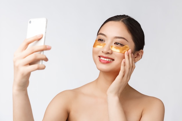 Close up selfie of beautiful happy woman with eye mask on faceWoman with eyes mask taking selfie with mobile phone at home enjoying relaxation and