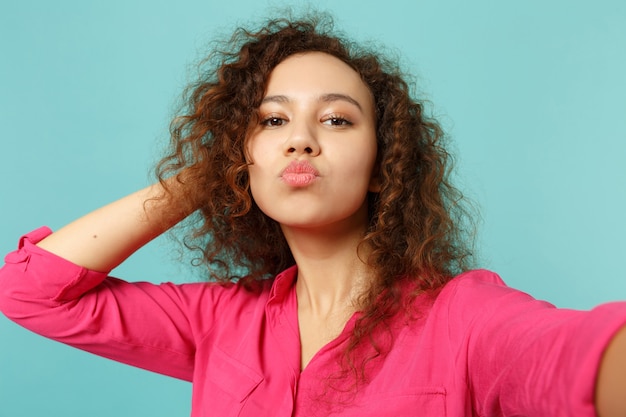 Photo close up selfie shot of pretty african girl in casual clothes blowing sending air kiss isolated on blue turquoise background in studio. people sincere emotions, lifestyle concept. mock up copy space.