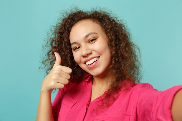 Close-up selfie shot van lachende afrikaanse meisje in casual kleding duim opdagen geïsoleerd op blauwe turquoise muur achtergrond in studio. mensen oprechte emoties, lifestyle concept. bespotten kopie ruimte.