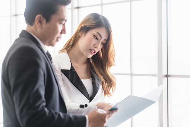 Close up senior asian businessman and young female\
businesswoman discuss in the office looking at a folder together\
focus on businessman