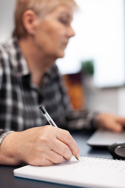 Close up of senior business woman writing notes on notebook