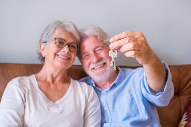 Close up of senior couple showing keys of house. Elderly couple holding keys for investment of property concept. Satisfied old couple holding keys to their new house