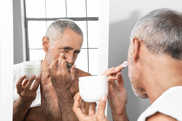 Foto uomo maggiore del primo piano che applica crema per il viso