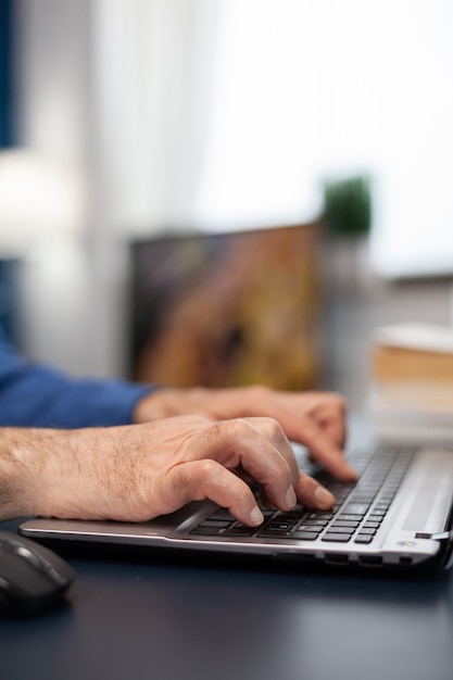 Close up of senior man hands typing on laptop keyboard elderly man entrepreneur in home workplace us...